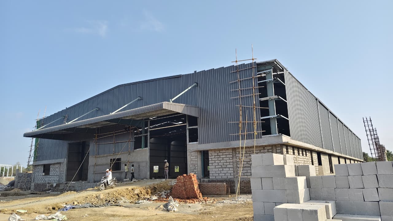 modern industrial PEB structure with large cantilevered canopy and insulated metal wall cladding, designed to IS/ AISC standards for heavy-duty storage.